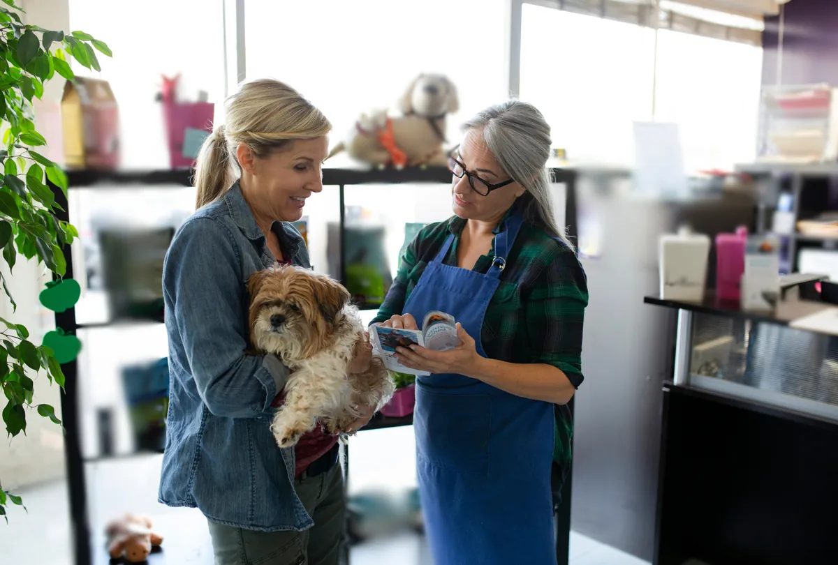 Woman holding fluffy Shih Tzu looking at colorful street dog art mural
