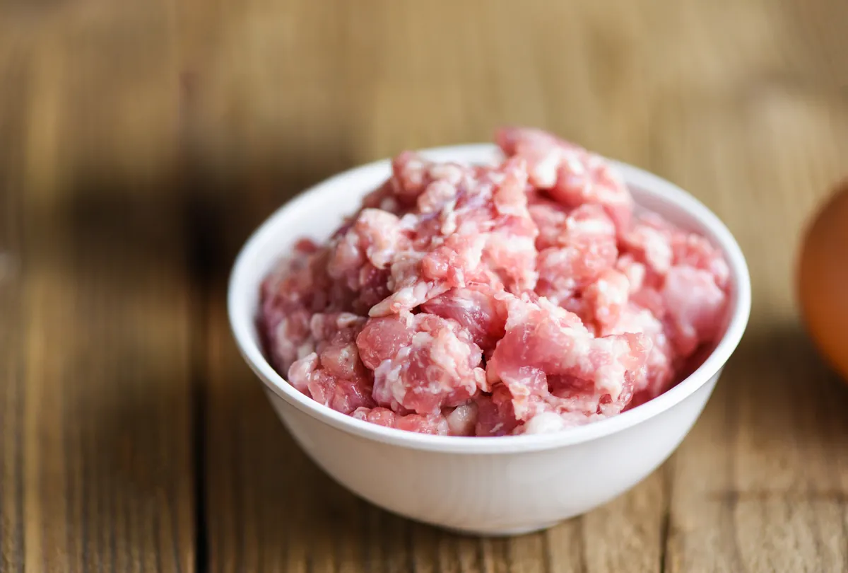 White bowl filled with raw pink dog food on wooden surface.