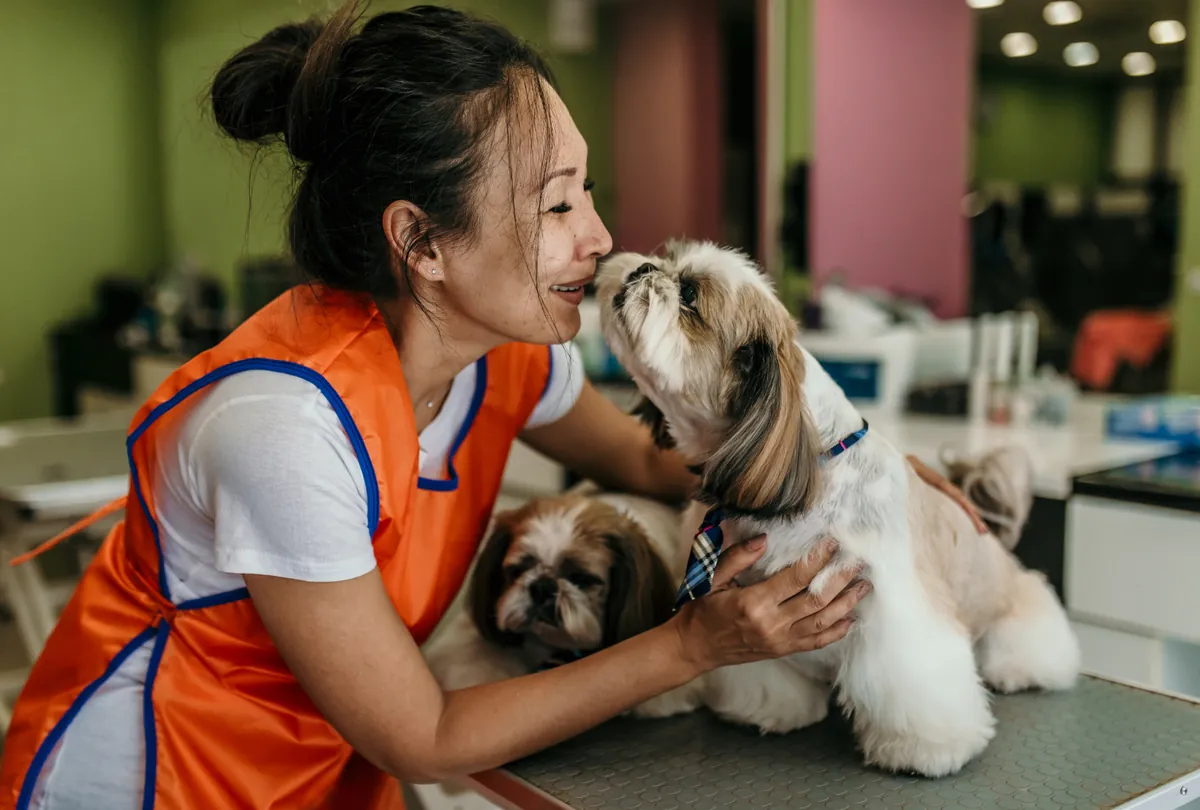 Woman in orange uniform holding white Shih Tzu at daycare.