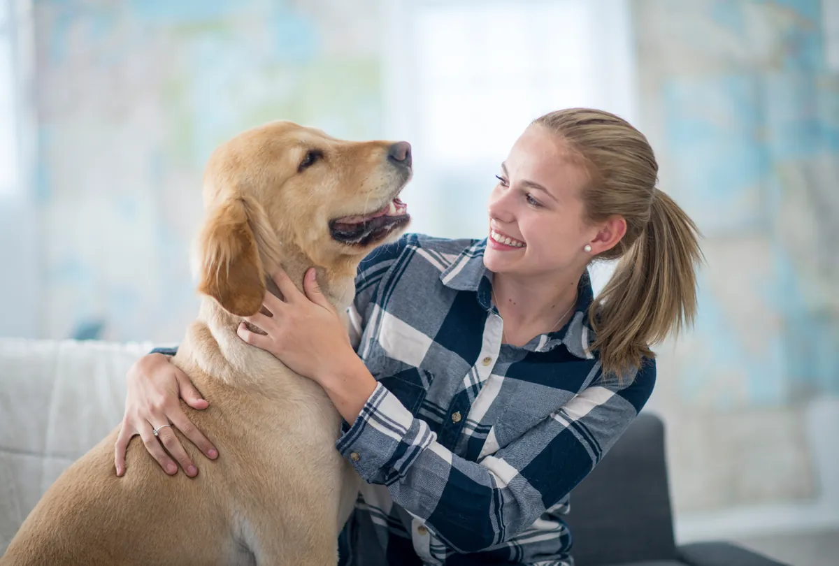 Blonde woman smiling at golden labrador in her arms indoors