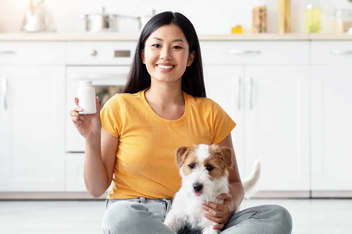 Woman holding pet supplement jar with small tan and white dog